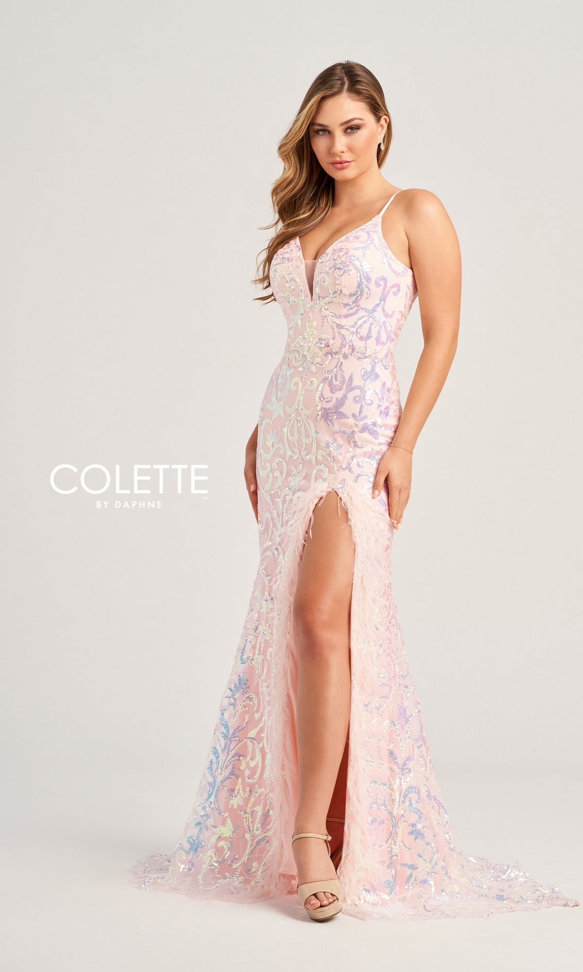 A woman models the Feather-Sequin Colette Long Prom Dress CL5155—a sleeveless, floor-length light pink gown with a deep V neckline and high slit. She pairs it with nude heels, standing against a simple backdrop.